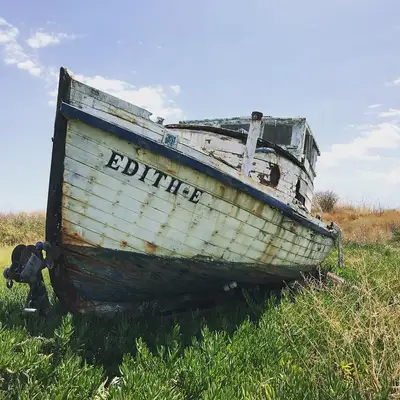 The weathered wooden fishing boat Edith-E resting in sunlit grass.