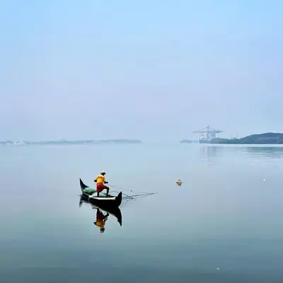 A lone person in a small boat reflected in still, pale blue water.